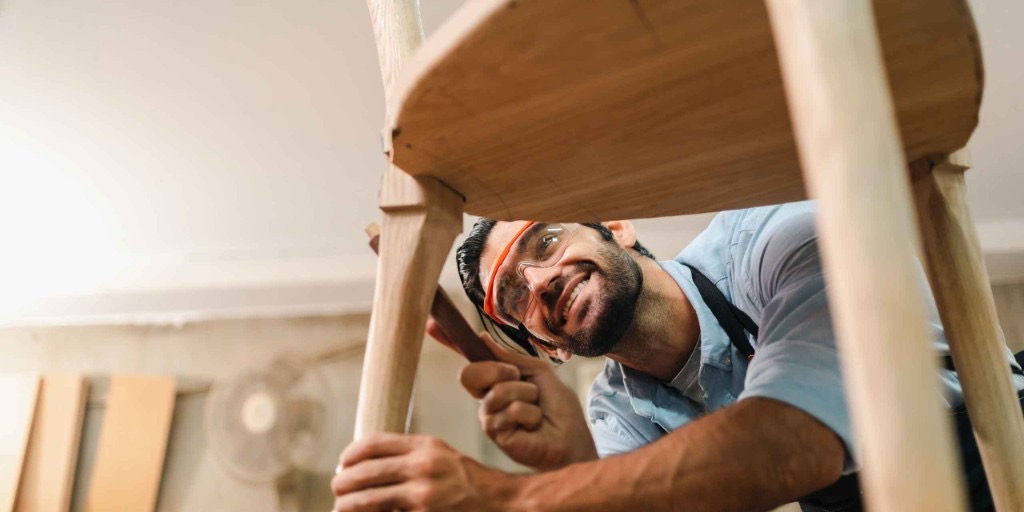 Carpenter refining joinery on a custom wooden chair in the workshop