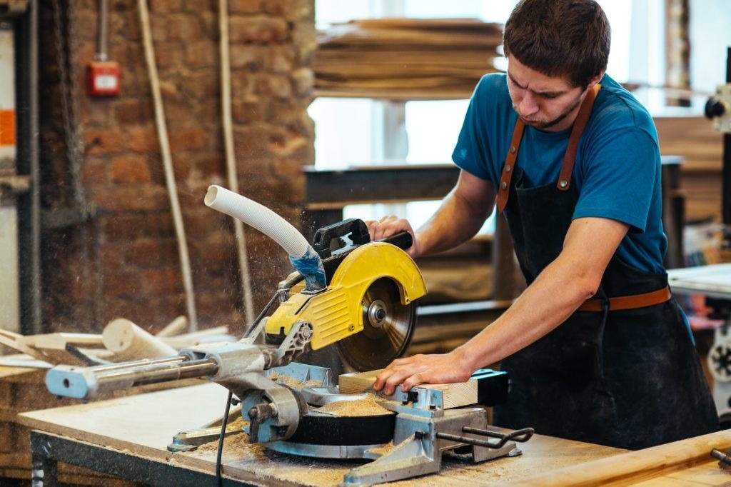 Craftsman cutting lumber with a yellow miter saw in the workshop
